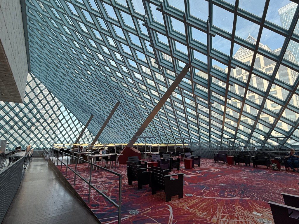 Interior view of the Seattle Central Library, featuring the distinctive glass and steel architecture with seating areas and a colorful carpet.