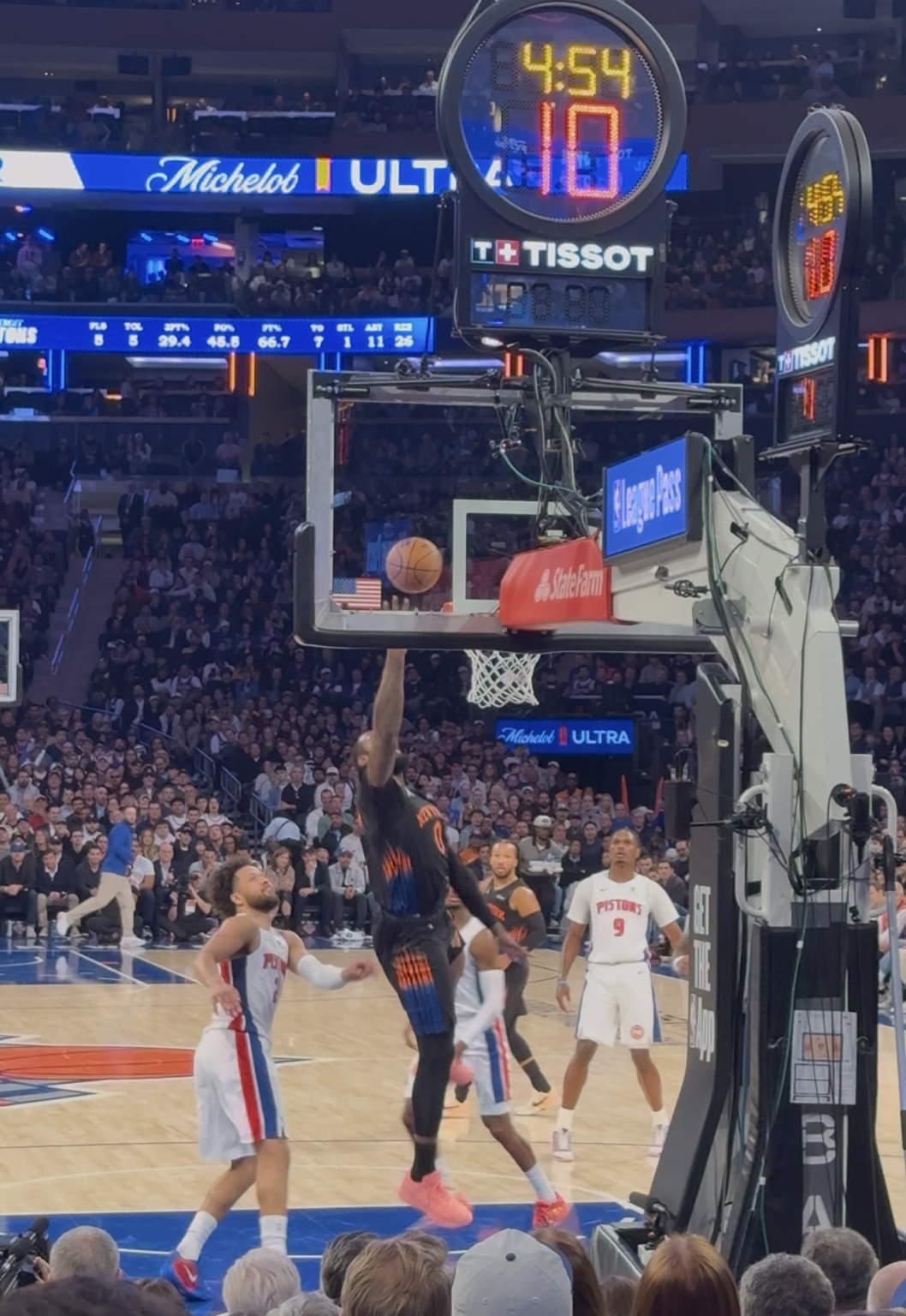 Andre Drummond reaching toward the rim for a tip-in with Pistons players beneath the basket.
