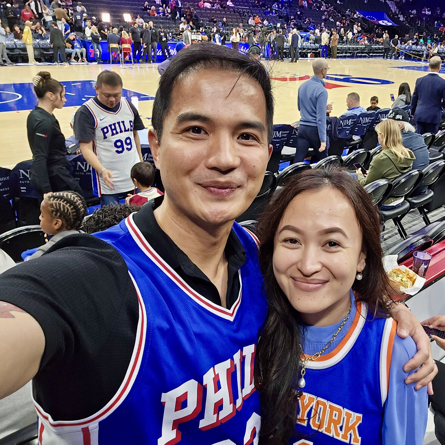 Frances and Francis in basketball jerseys courtside at an NBA game in Philadelphia