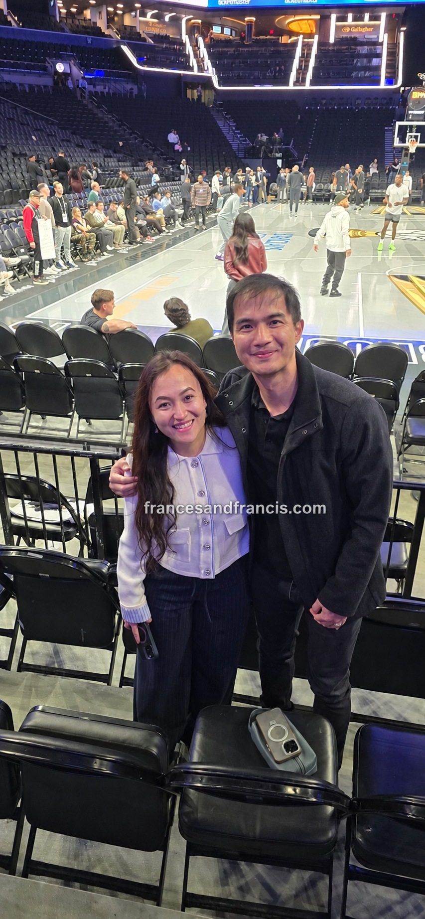 Frances and Francis beside their seats, with courtside chairs and the basketball court directly behind them at Barclays Center.